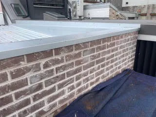 Brick parapet wall with white efflorescence staining across the upper courses before cleaning